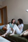 Восхитительные лесбиянки сидят вместе на диване в гостиной и смотрят друг на друга — стоковое фото