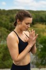 Jeune femme consciente en vêtements de sport méditant avec les yeux fermés tout en pratiquant le yoga dans la nature — Photo de stock