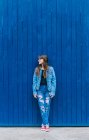 Moda hipster feminino vestindo jaqueta de ganga e jeans encostados na parede azul na rua da cidade e olhando para longe — Fotografia de Stock