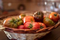 Haufen frischer Tomaten in Weidenkorb in der rustikalen Küche in der Erntezeit auf den Tisch gestellt — Stockfoto