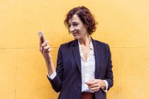 Selbstbewusste elegante Frau in formalem Outfit, die auf den Bildschirm ihres Mobiltelefons blickt — Stockfoto
