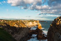 Cenário espetacular de costa rochosa áspera lavada por ondas marinhas espumosas sob a luz solar sob o céu azul nublado em Liencres Cantabria, na Espanha — Fotografia de Stock