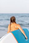 Rückenansicht einer nicht wiedererkennbaren Frau im Badeanzug, die im Sommer mit SUP-Board im Meerwasser steht — Stockfoto