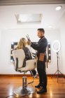 Homme coiffeur à l'aide de fer à friser serrures blondes de cliente pendant le travail dans un salon de beauté — Photo de stock