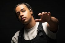 Handsome young ethnic male with Afro braids dressed in black and white clothes looking at camera while sitting in dark studio — Stock Photo