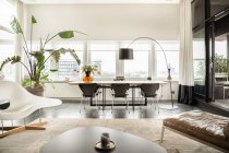 Interieur eines modernen, geräumigen Wohnzimmers mit bequemem Sofa und Holztisch und -stühlen in einer modernen, luxuriösen Wohnung mit Panoramafenstern — Stockfoto