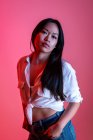 Seitenansicht des selbstbewussten ethnischen weiblichen Modells in trendiger Kleidung mit Blick auf die Kamera im Studio auf rosa Hintergrund — Stockfoto