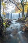 Vista panorámica de la cascada que desciende por rocas en bosques montañosos en otoño en larga exposición en el río Lozoya en el Parque Nacional Guadarrama - foto de stock