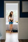 Чарівна струнка жінка одягає джинсові шорти, стоячи в спальні вдома — стокове фото