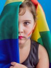 Nettes Mädchen mit roten Lippen und Regenbogenfahne, die den halben Kopf bedeckt und in die Kamera auf blauem Hintergrund schaut — Stockfoto