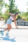 Side view of fit cheerful female in headphones and in rollerblades showing stunt on road in city in summer — Stock Photo