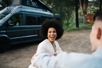 Femme afro-américaine souriante tenant la main du petit ami cultivé tenant la main tout en se promenant et en regardant loin contre le camping-car — Photo de stock