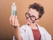 Поразительный мальчик в очках и лабораторном халате с грязным лицом и жидкостью в бутылке после химического эксперимента — стоковое фото