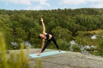 Full body female in sportswear doing Triangle pose on rock during yoga session on summer day in nature — Stock Photo