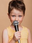 Cool enfant dans le chant en micro moderne sur fond brun en studio — Photo de stock