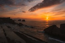 Incredibile scenario tranquillo del tramonto sul mare ondulato increspato con rocce sotto cielo nuvoloso colorato in estate sera a Liencres Cantabria Spagna — Foto stock
