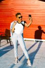 Веселая афроамериканка в модном костюме, разговаривающая по мобильному телефону, глядя в солнечный город — стоковое фото