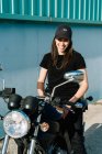 Позитивний жіночий мотоцикліст сидить на мотоциклі, припаркованому на вулиці міста в сонячний день і дивиться на камеру — стокове фото