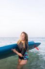 Feminino de maiô de pé com prancha SUP na água do mar no verão e olhando para longe — Fotografia de Stock