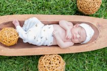 Draufsicht auf das süße kleine Neugeborene, das schläft, während es in einer Holzwanne auf grünem Gras liegt — Stockfoto