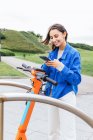 Зміст жінки, що орендує припаркований електричний скутер у місті та перегляд мобільного телефону — стокове фото