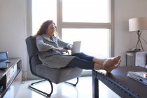 Вид сбоку на деловую женщину с кудрявыми волосами, сидящую на диване и работающую с ноутбуком — стоковое фото