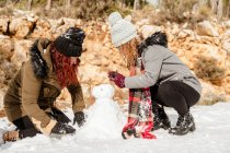 Вид збоку на жінок у верхньому одязі, які роблять сніговика в лісі та розважаються разом у вихідні — стокове фото