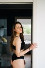 Вид збоку на спокусливу жінку в чорній білизні, що стоїть у дверному отворі спальні вдома — стокове фото