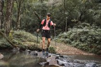 Männlicher Wanderer mit Trekkingstöcken steht in Waldnähe am See — Stockfoto
