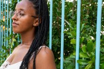 Ruhige afroamerikanische Hündin mit langen geflochtenen Haaren steht im Sommer am Zaun im grünen Garten und genießt die Natur mit geschlossenen Augen in Barcelona — Stockfoto