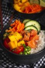 Hohe Winkel der asiatischen Poke mit Lachs und Reis mit verschiedenen Gemüse serviert in Schüssel auf dem Tisch mit Essstäbchen im Restaurant — Stockfoto