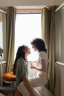 Вид сбоку на содержание ЛГБТ пара влюбленных женщин на диване дома и смотрят друг на друга с любовью — стоковое фото