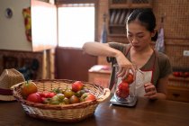 Focused ethnic housewife weighing fresh tomatoes in glass jug on kitchen scale while cooking food at home — Stock Photo