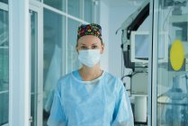 Веселая взрослая женщина-медик в стерильной маске и декоративной кепке, смотрящая на камеру в больнице — стоковое фото