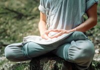 Cropped unrecognizable man in traditional clothes sitting on rock in Lotus pose and meditating during kung fu training in forest — Stock Photo