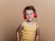 Soddisfatto preteen boy in cuffie rosse ascoltare musica su sfondo marrone in studio — Foto stock