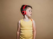 Zufriedener Frühchen-Junge mit roten Kopfhörern hört Musik auf braunem Hintergrund im Studio — Stockfoto