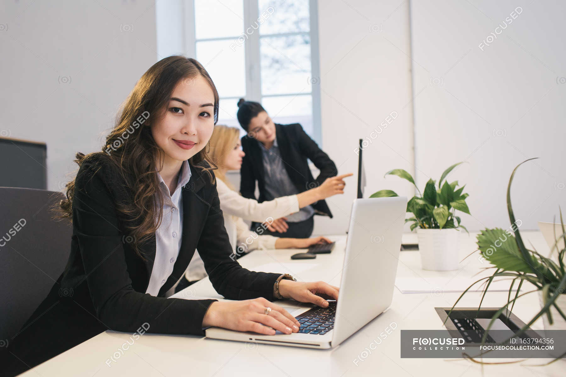 Young Office Worker Sitting At Desktop In Office And Smiling At Camera 