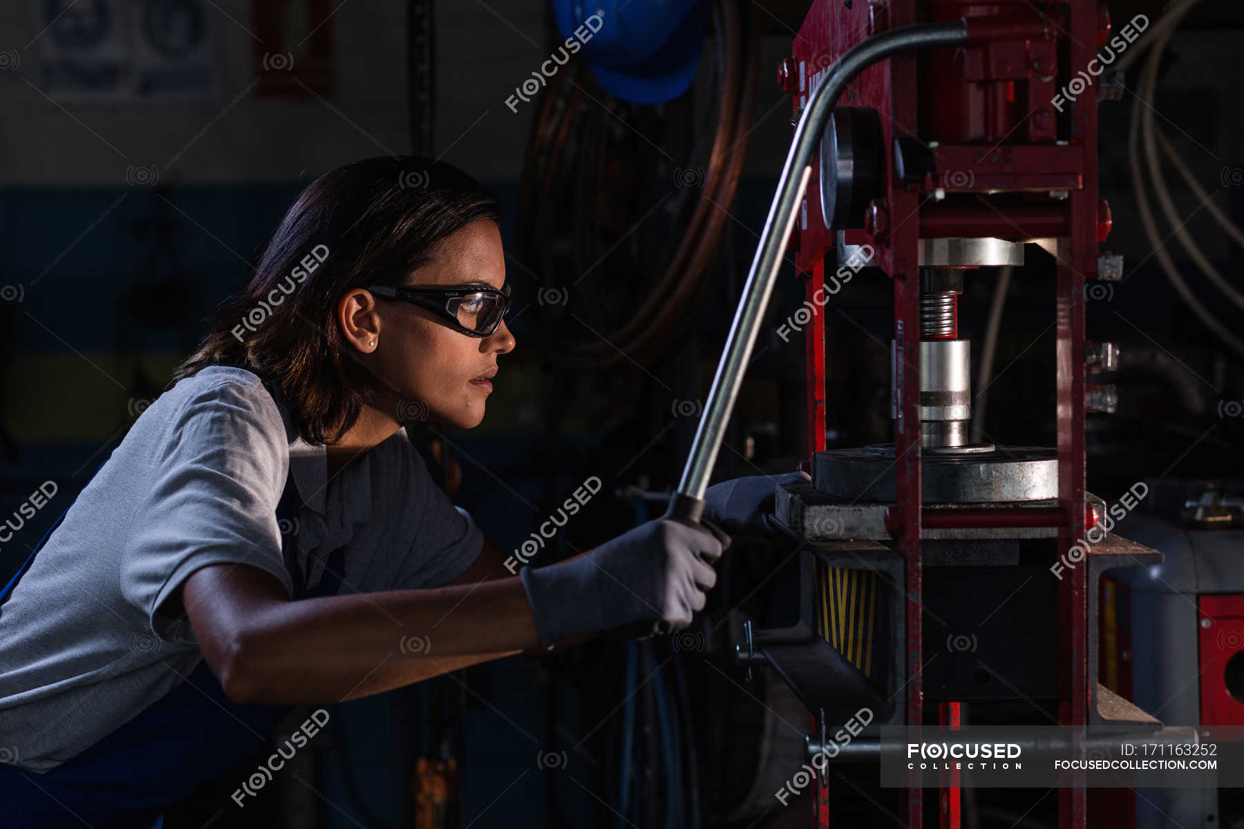 Side view of female mechanic in protective googles operating hydraulic ...