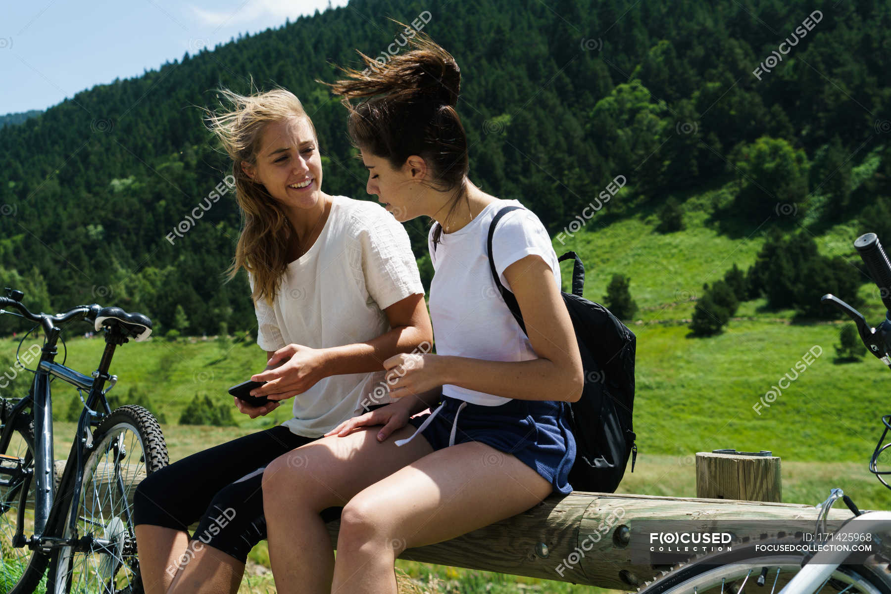 Ragazze sedute con le biciclette e utilizzando smartphone — amici 