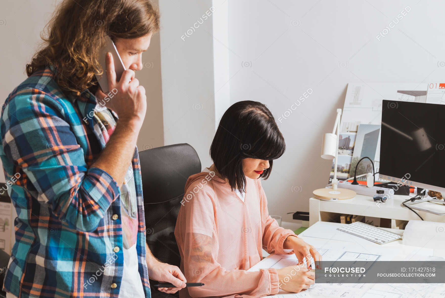 Seitenansicht Eines Mannes Der Telefoniert Und Eine Frau Ansieht Die Im Buro Eine Blaupause Entwirft Architektonisch Designer Stock Photo 171427518