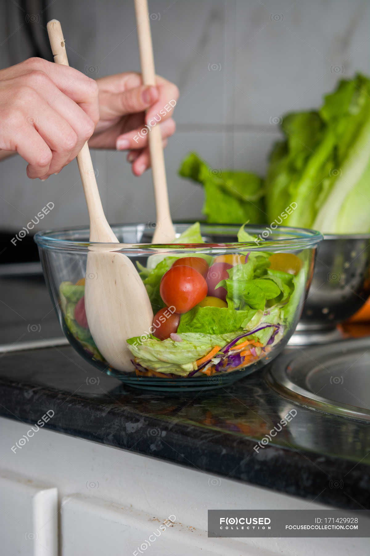 Cropped image of hands mixing salad in bowl at kitchen counter