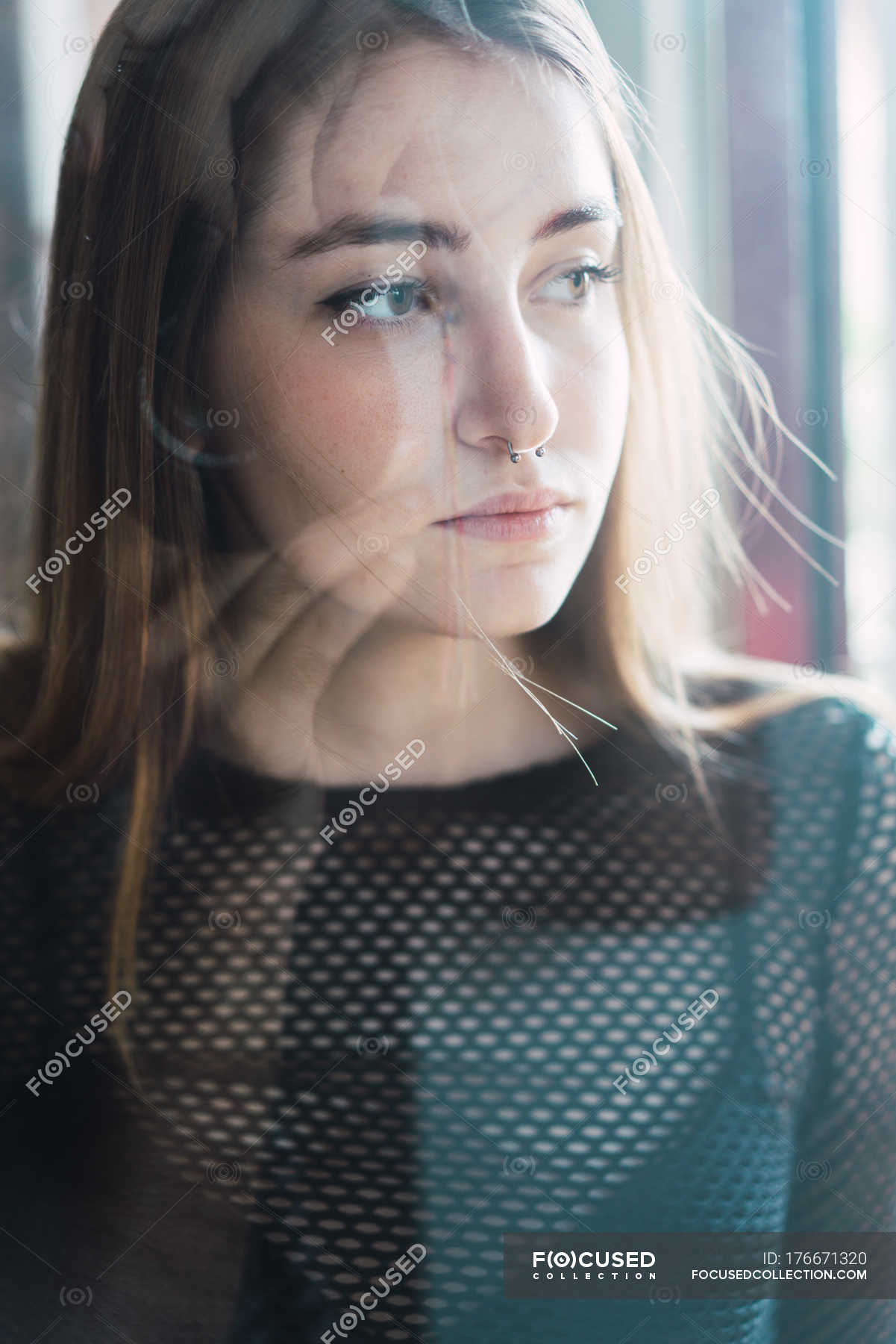 Portrait of young girl with piercing posing pensively behind glass and ...