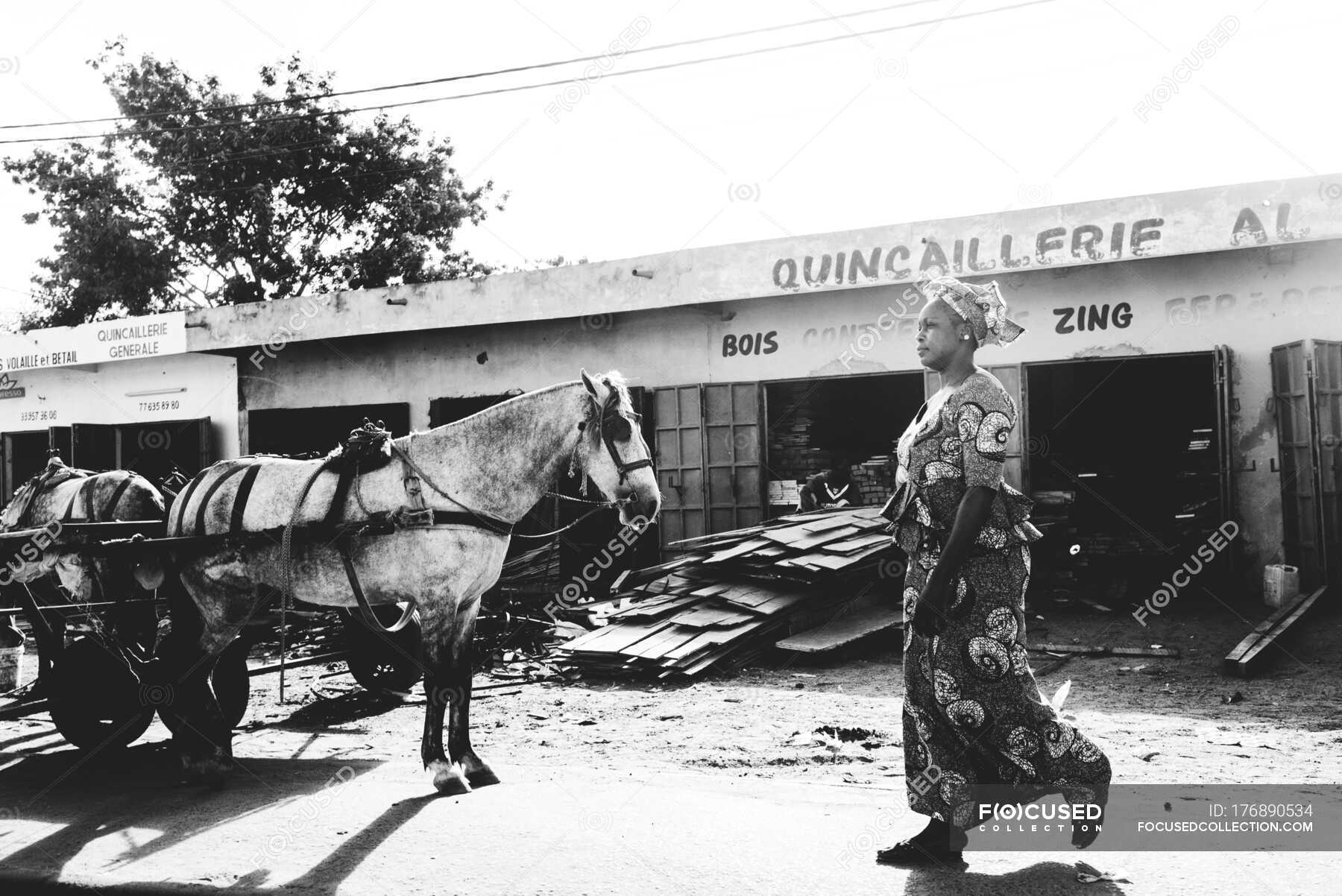 African woman in traditional clothes walking along street near horse ...