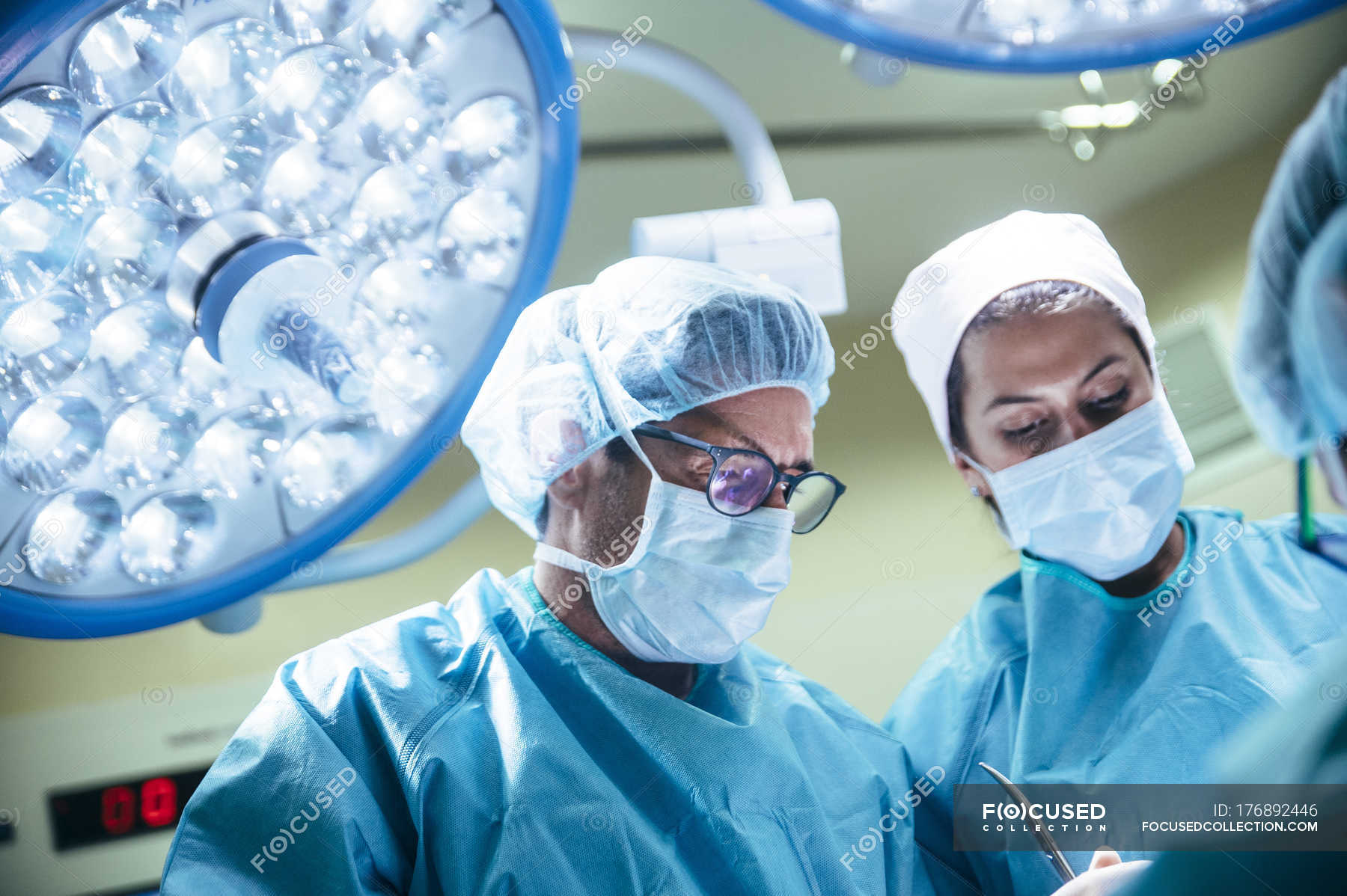 Portrait of doctors in masks looking down at patient in surgery room ...