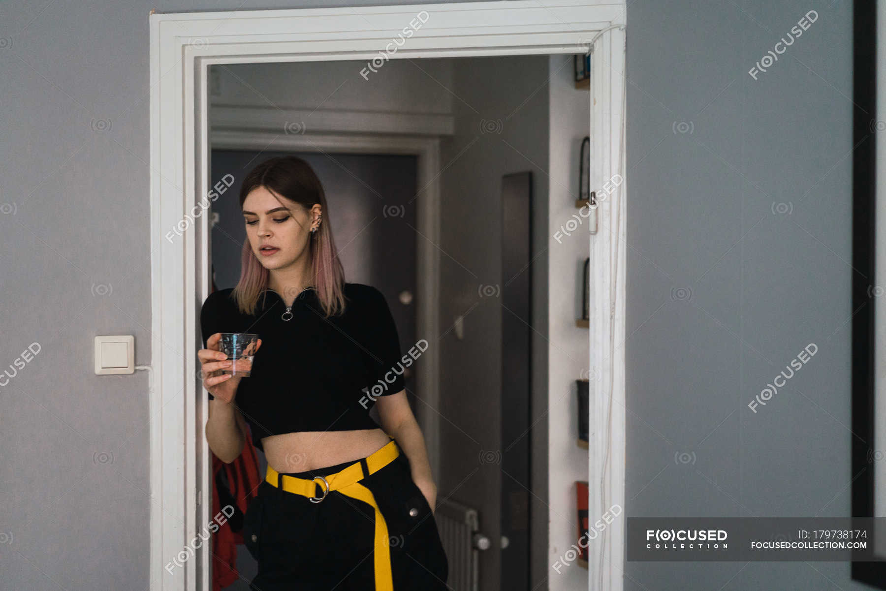 Portrait Of Young Woman Standing In Doorway With Glass Of Water And Looking Down — House Copy 7852