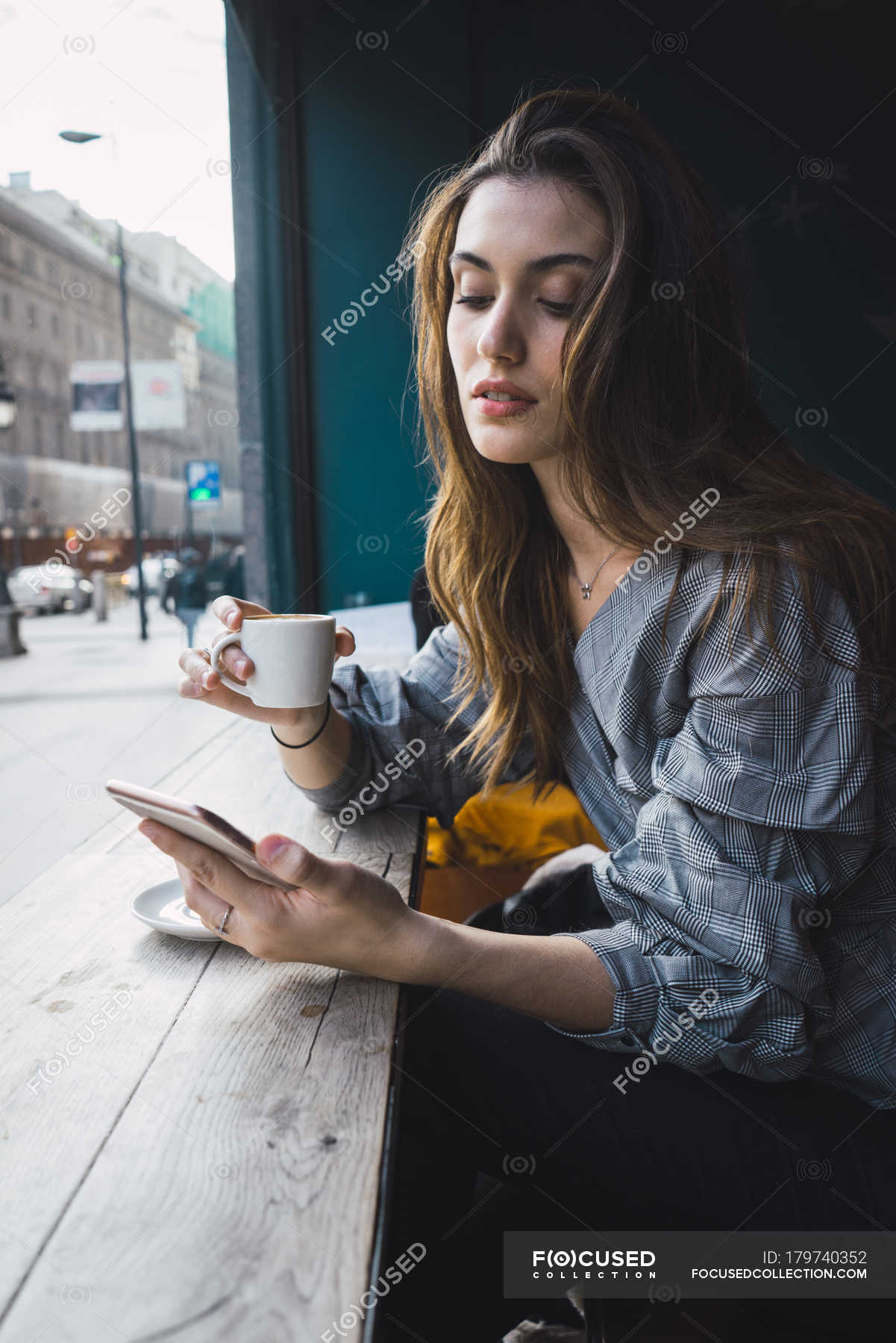 Portrait of brunette girl drinking coffee at cafe and browsing