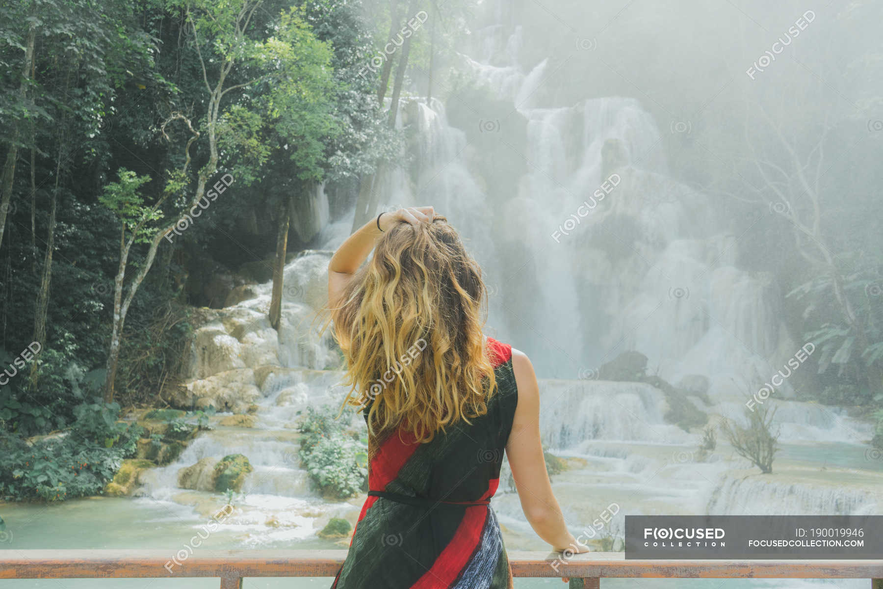 Back View Of Blonde Woman Holding Hair And Looking At Cascade From