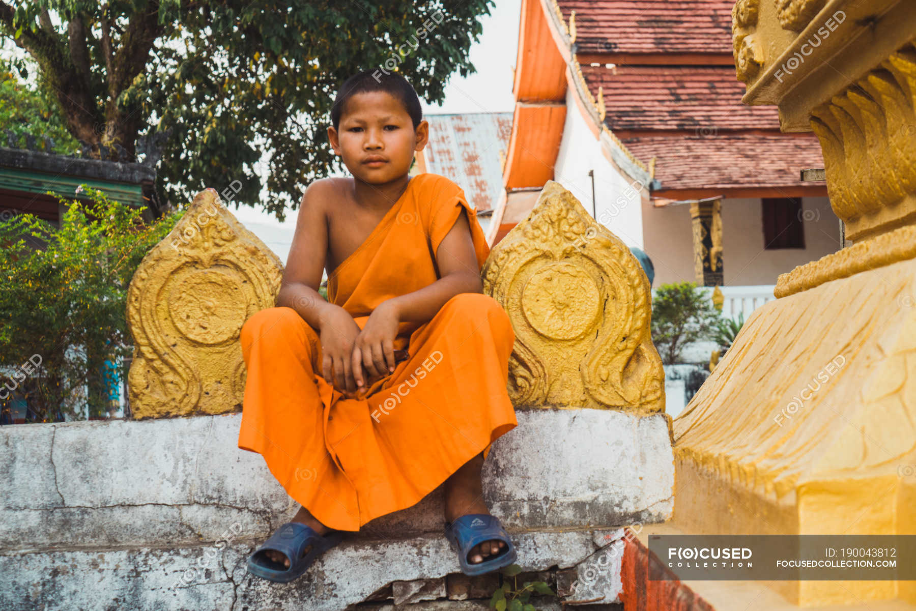 LAOS- FEBRUARY 18, 2018: Little boy monk sitting on fence and looking ...