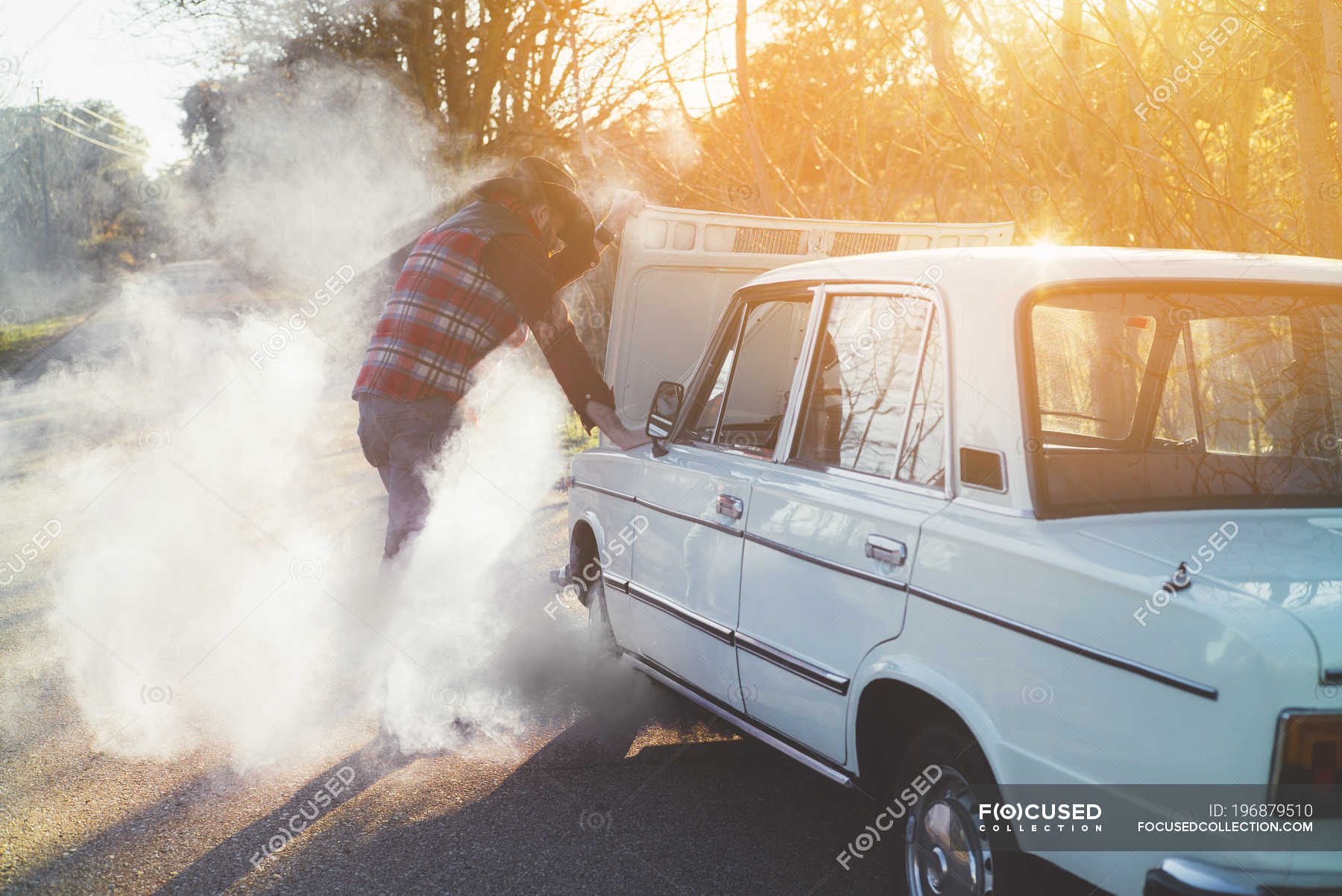 Side view of man opening hood of smoking car in nature. — classic
